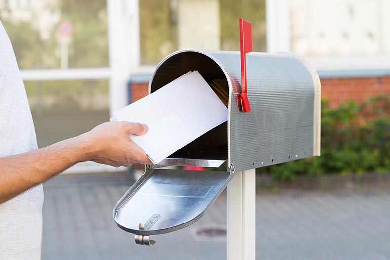 Close-up of a 55+ person putting a stack of letters in the mailbox.