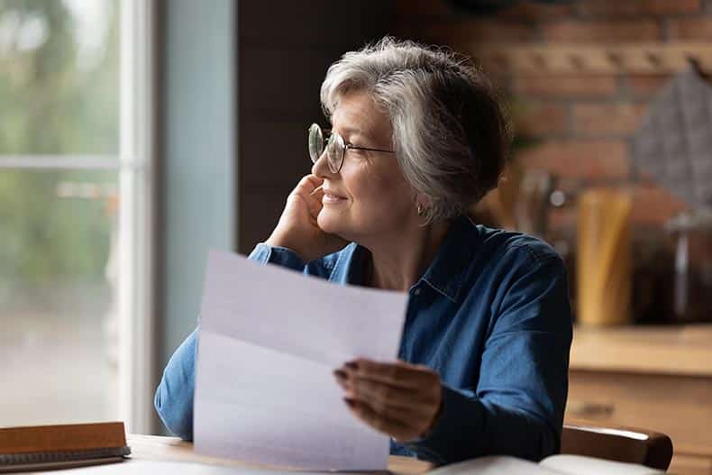 A thoughtful 55+ woman holding a letter from her homeowners' association.