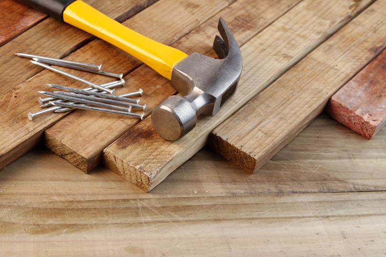 A hammer beside a pile of nails on a stack of wood.