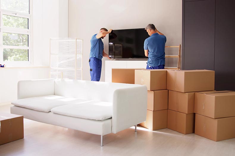 Two young male movers in uniform placing a television in a home.