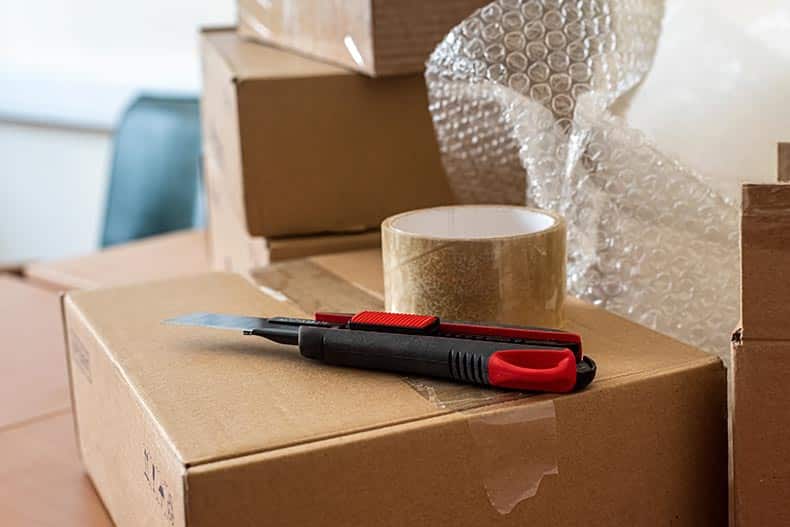 A box knife and sticky transparent tape on a packing box.