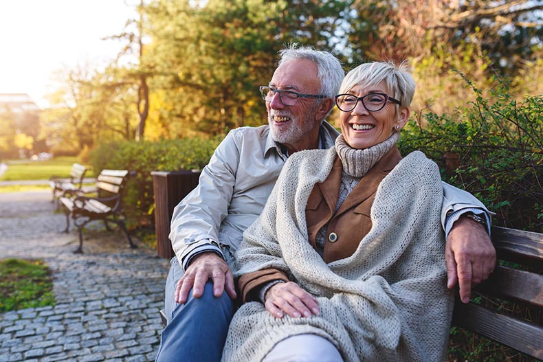 A smiling senior couple sitting on the bench in their 55+ community.