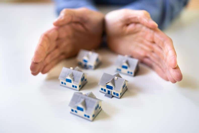 Hands protecting miniature houses on a desk.