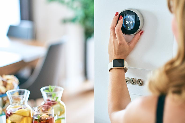 A 55+ woman adjusting the thermostat in her home.