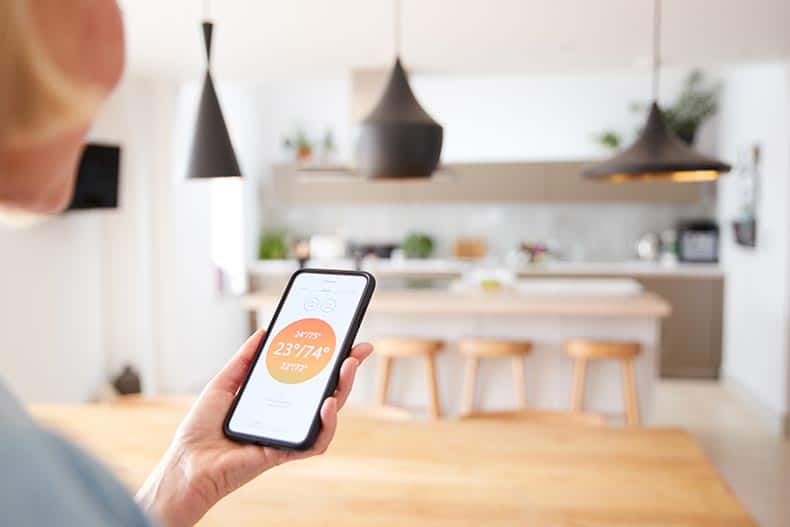 Closeup of a 55+ woman using an app on her smart phone to control her house thermostat.