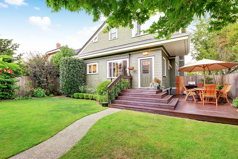 A backyard area with walkout deck, patio table set, and well kept lawn.