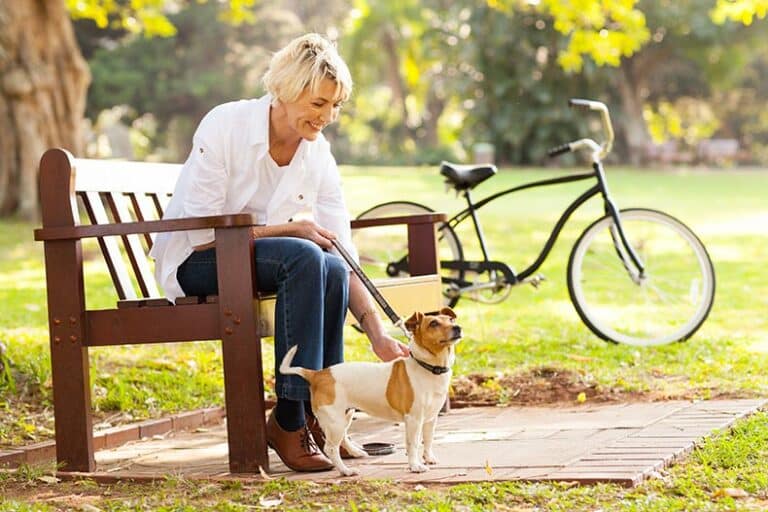 A happy 55+ woman with her dog in a dog park.