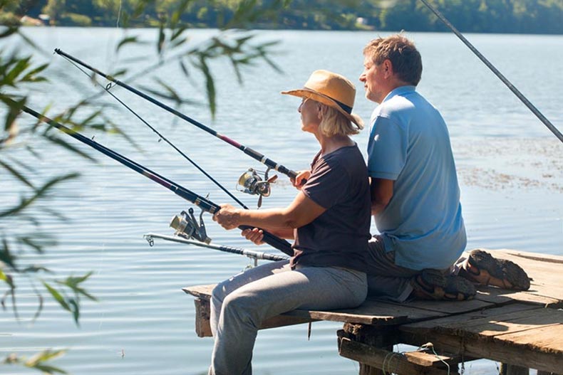 An older couple sitting on the end of a dock and fishing.