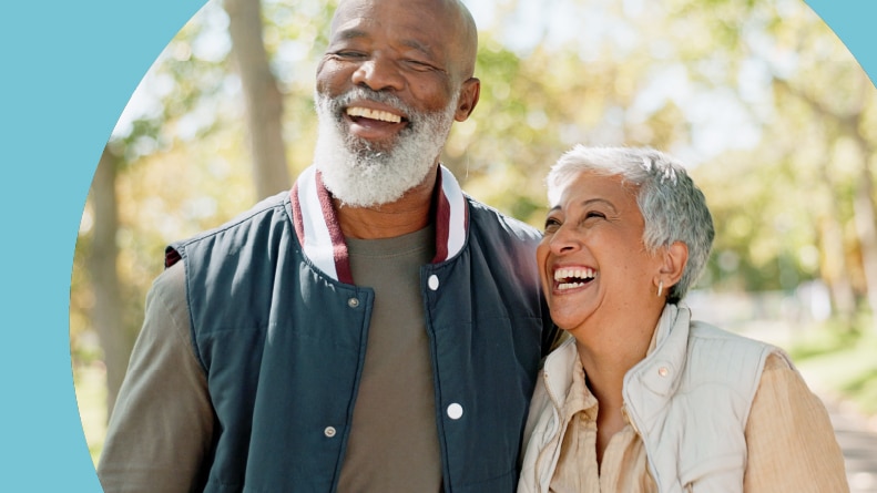 An active adult couple smiling and walking in a park in their 55+ community.