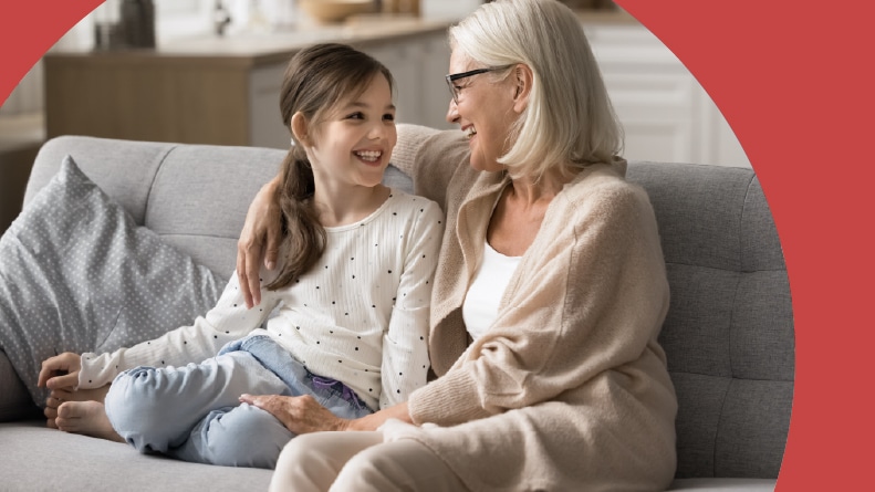 A cheerful loving grandmother and a granddaughter talking and laughing on a sofa.