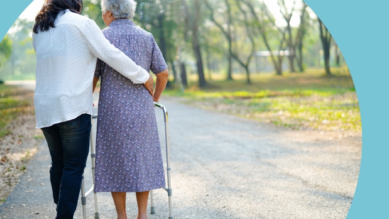 A young woman helping a senior woman with a walker in a park.