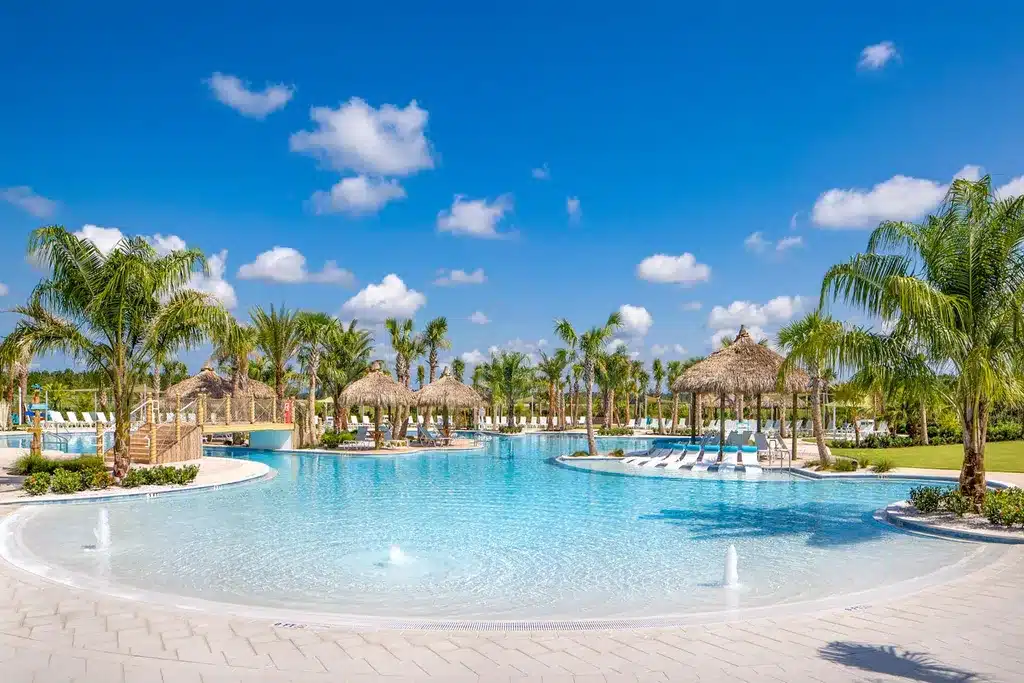 View of the resort-style pool with tiki huts and palm trees at Latitude Margaritaville. 