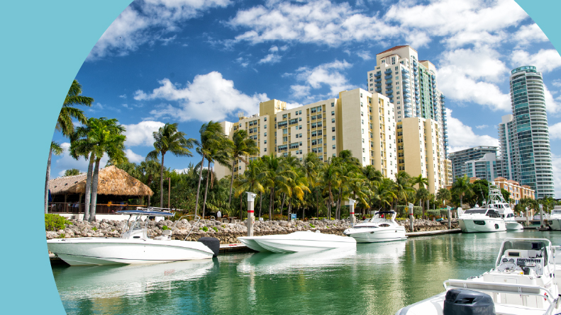 The Miami Beach coastline with hotel buildings, white boats, and green palm trees.