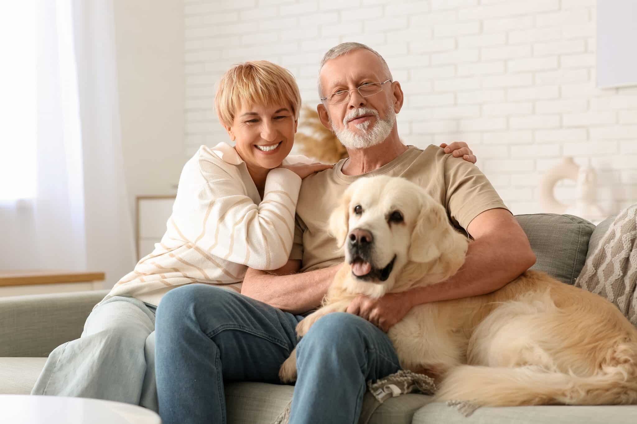 Older couple cuddle together on a couch with their large white dog.