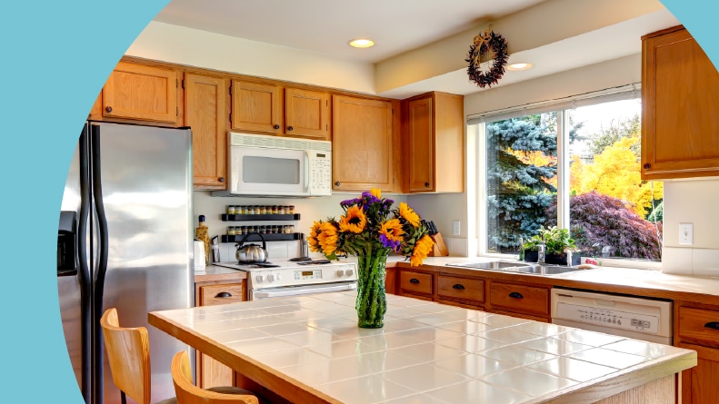 A cozy kitchen with honey-colored cabinets, white appliances, and kitchen island with fresh flowers.