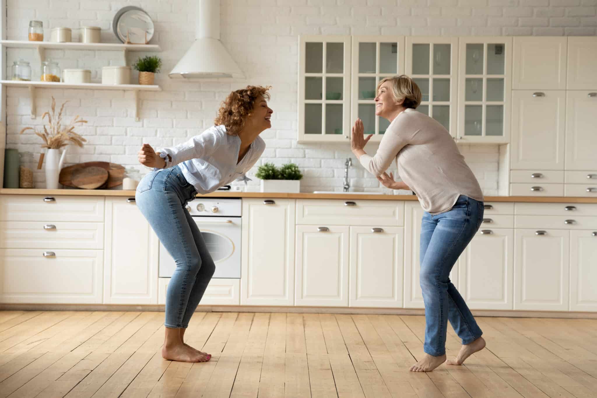 Older mother and daughter dancing together in the kitchen.