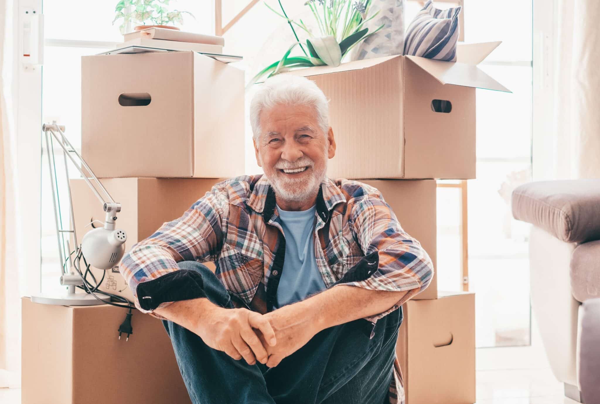 Senior man smiling and sitting in front of moving boxes.
