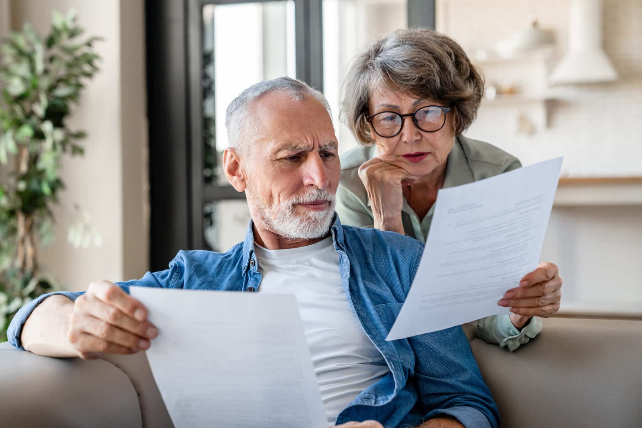 Senior couple looking at paper work together on the couch.