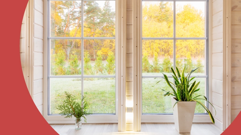 The bright interior of a room in a wooden house with a large window overlooking the yard.