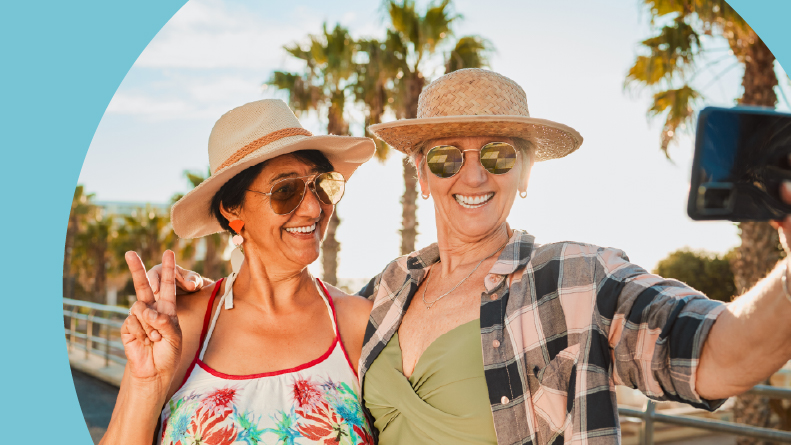 Two 55+ women smiling while taking a selfie near the beach.