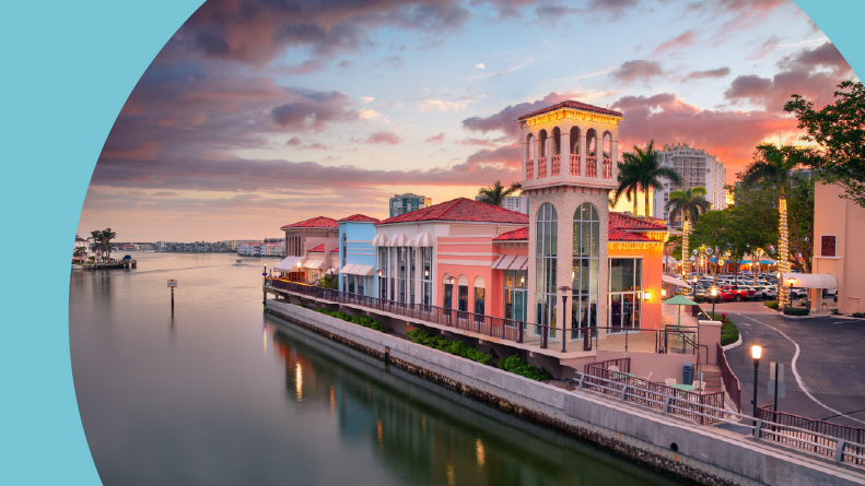 The cityscape of Naples, Florida with the reflection of the city skyline in the water at sunset.