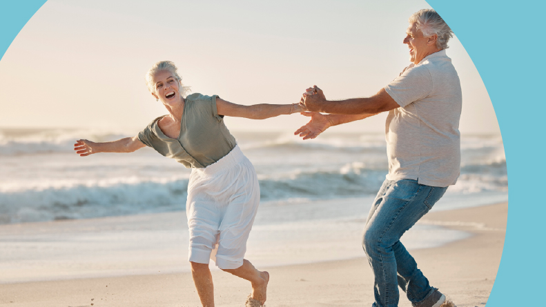 A 55+ couple smiling and laughing while playing on a beach in Florida.