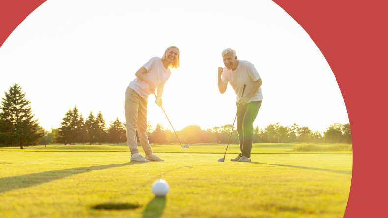 A 55+ couple playing golf on a course at sunset.