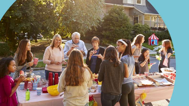 Neighbors talk and eat around a table at a block party.