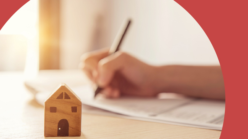 Close-up of a wooden toy house and a woman signing a lease.