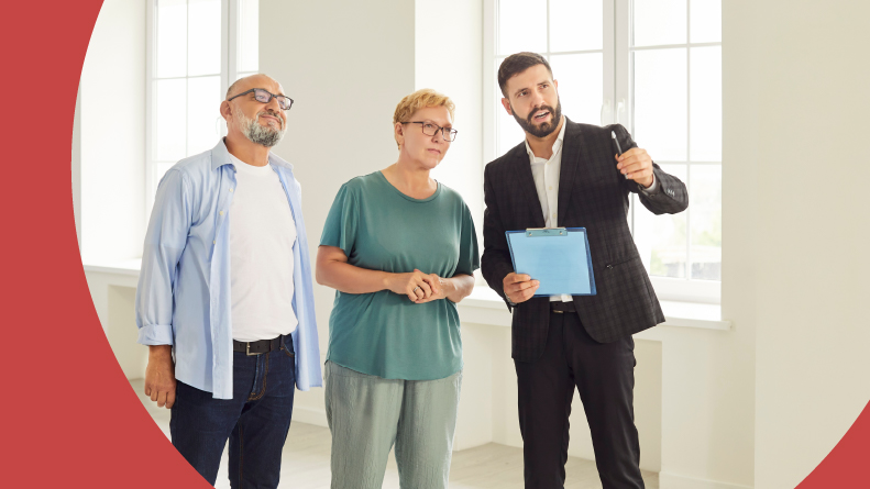 A senior couple listens to a real estate agent in an empty apartment.