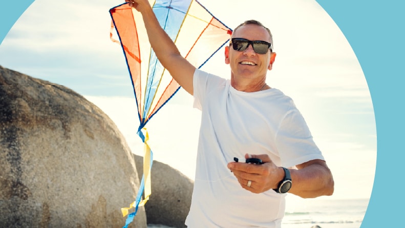 A single 55+ man holding a kite while at the beach.