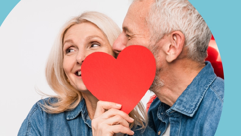 A loving 55+ couple holding a red paper heart.