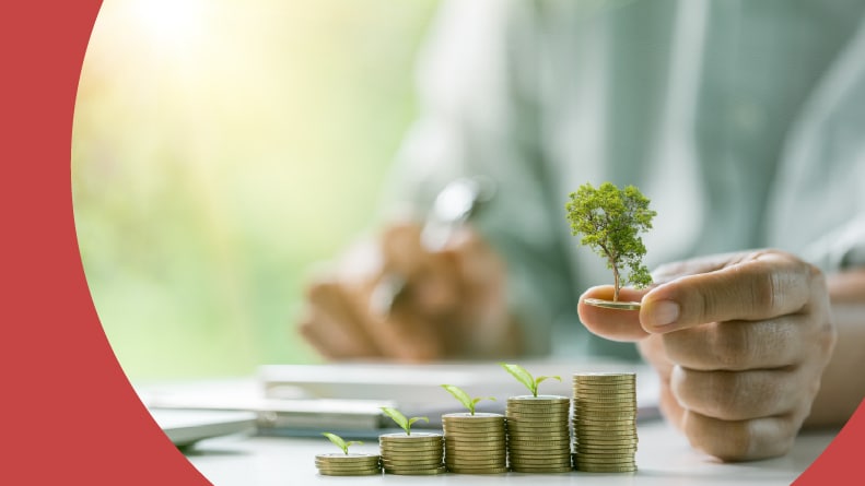 A hand lifting a coin from a stack of coins growing small sprouts.
