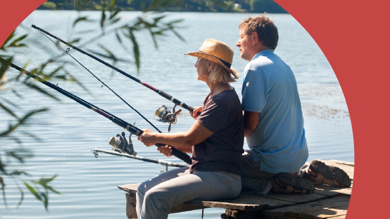 An older couple sitting on the end of a dock and fishing.