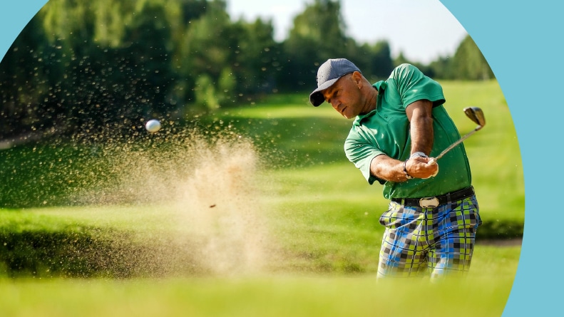 A golfer hits a ball from a bunker with a golf club.