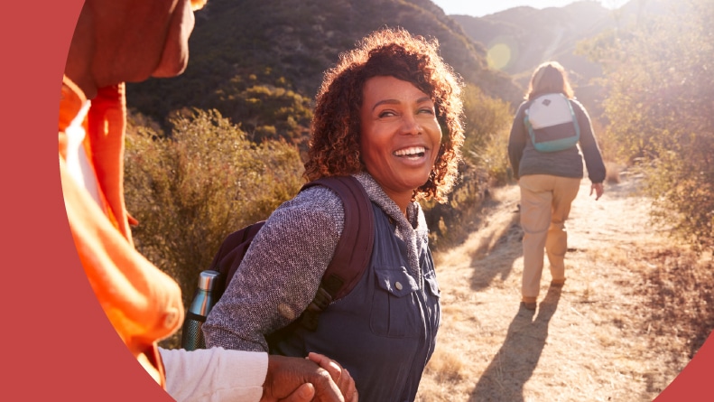 An older woman holding her partner's hand as they head down a nature trail with a hiking group.