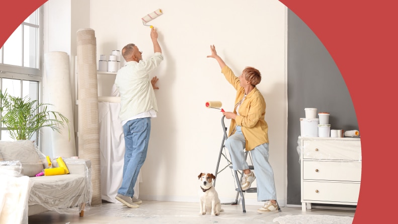 A mature couple with a dog painting a wall in their house.