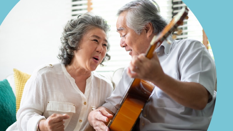 A senior couple sitting on a couch while singing and playing acoustic guitar together.