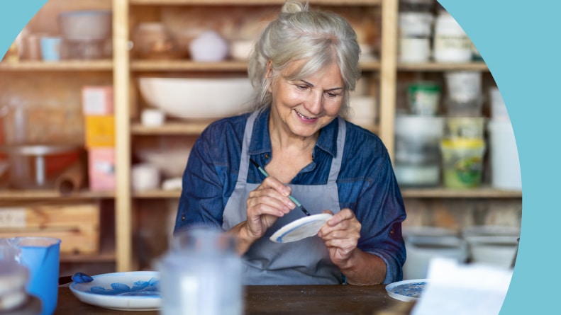 A senior craftswoman painting a clay plate in an art studio.