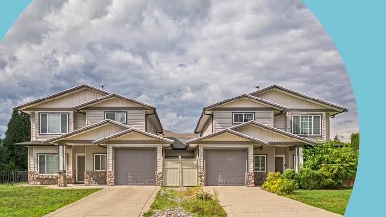 Residential duplex building with concrete driveway and green lawn in front.