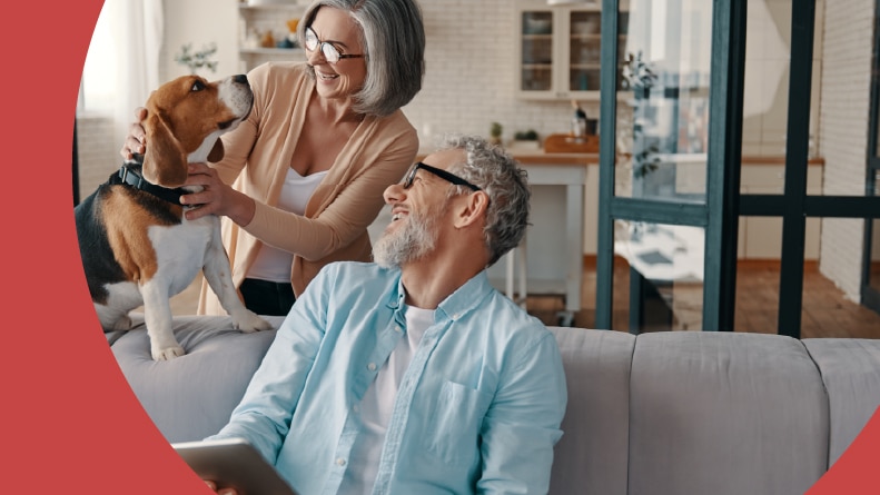 A 55+ couple smiling and taking care of their dog while at home.