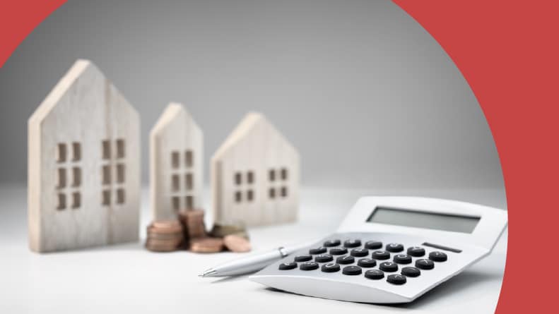 A calculator beside wooden houses and a stack of coins.