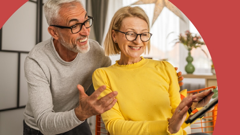 A happy 55+ couple browsing homes for sale on a tablet together.