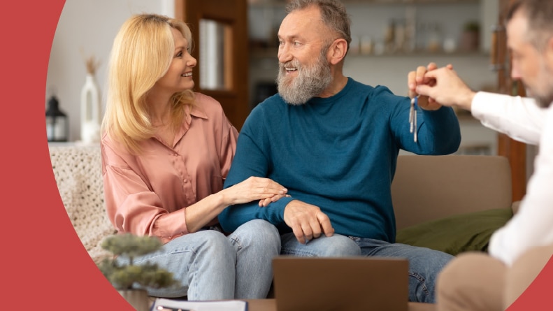 A 55+ couple receiving the keys to their new house from a real estate agent.