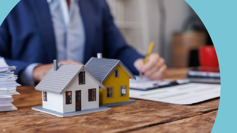 Small house models beside a real estate agent filling out homebuying paperwork.
