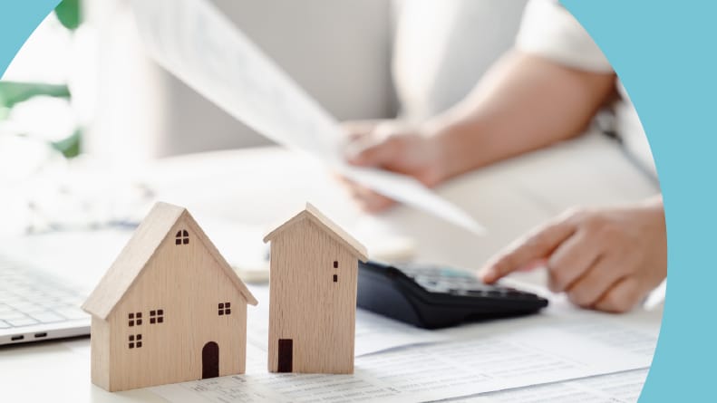 A 55+ woman calculating home loan payments using a calculator and a laptop.