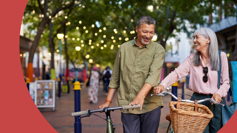 A 55+ couple smiling and laughing while walking their bicycles.
