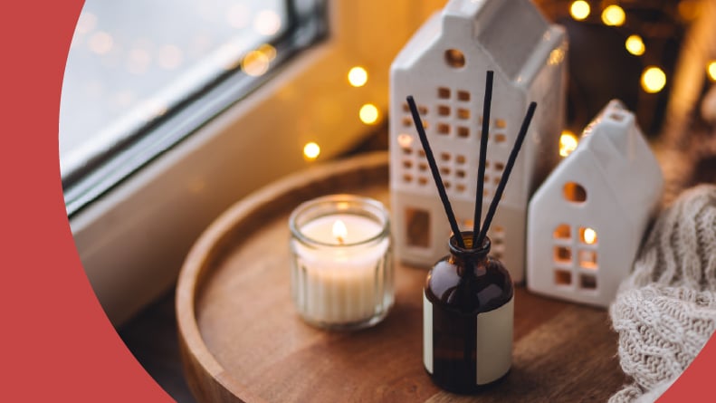 An aroma diffuser and a burning candle on a wooden bamboo tray beside aknitted sweater.