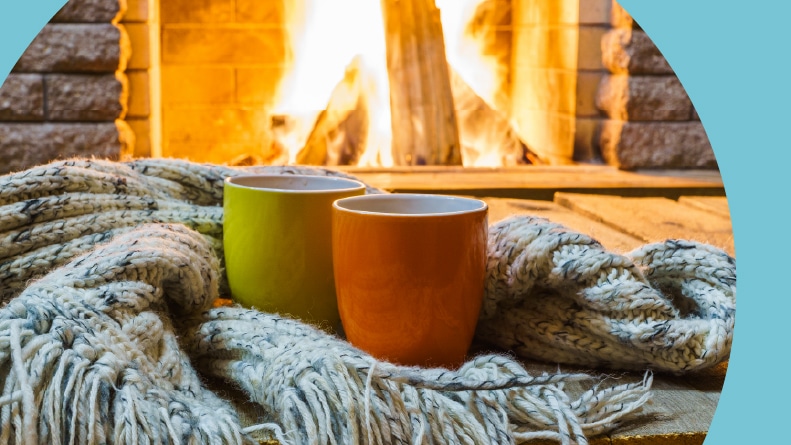 Two mugs for tea or coffee beside a wool scarf near a cozy fireplace.