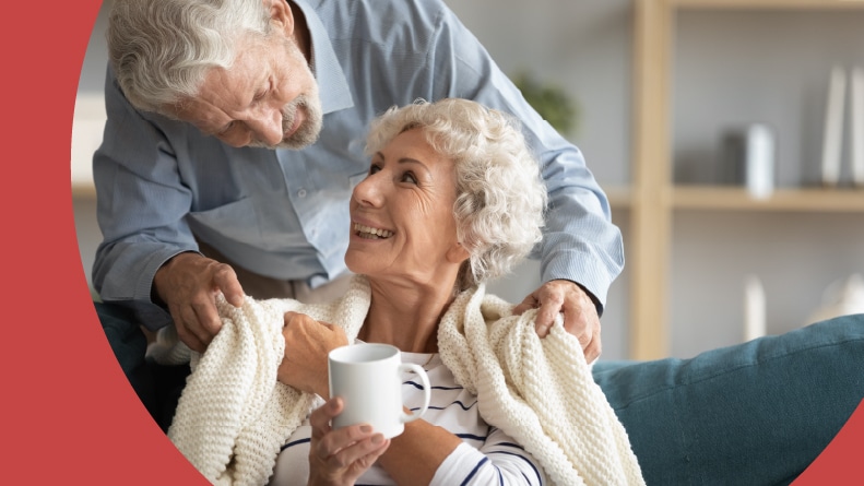 A 55+ man putting a blanket over his wife's shoulders during the winter.